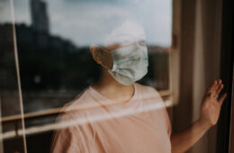 马来西亚实施行动限制令期间，一名亚裔华人女性戴着口罩从阳台窗口向外看