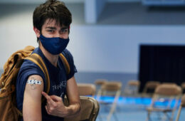 图为一名学生在CWRU疫苗诊所指着他手臂上的绷带