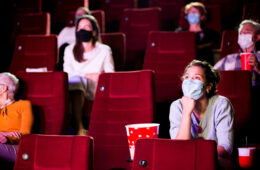 戴着面具和身体上保持距离的人坐在电影院的照片