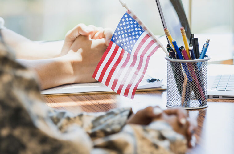 一个穿着军装的人坐在桌子前，铅笔托里插着一面美国国旗