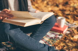 在秋天的花园里，年轻女子坐在毯子上，看书，喝咖啡或茶