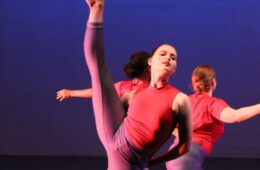 一个舞者用尖脚趾踢她的腿的特写，另一个表演者在背景中。