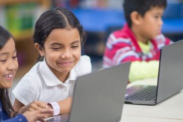 在计算机实验室里，一群来自不同民族的小学生正在用笔记本电脑一起学习。